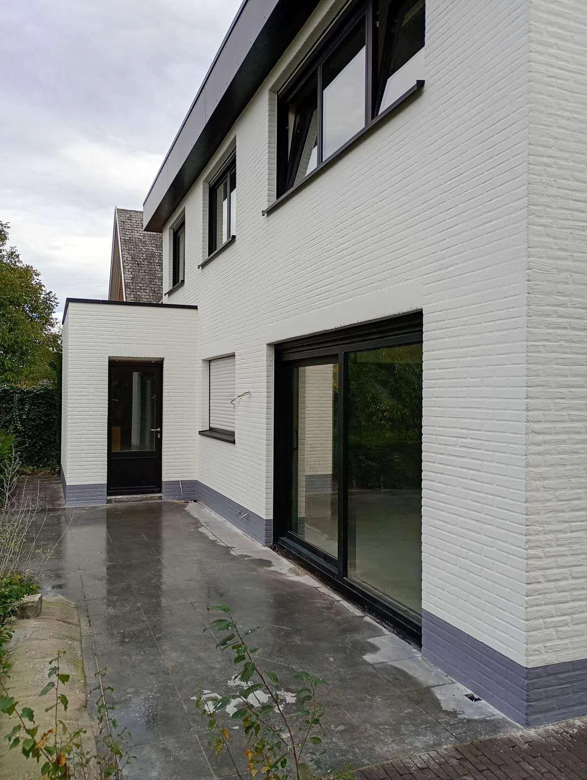 Lichte steenstripgevel met donkere ramen en plint